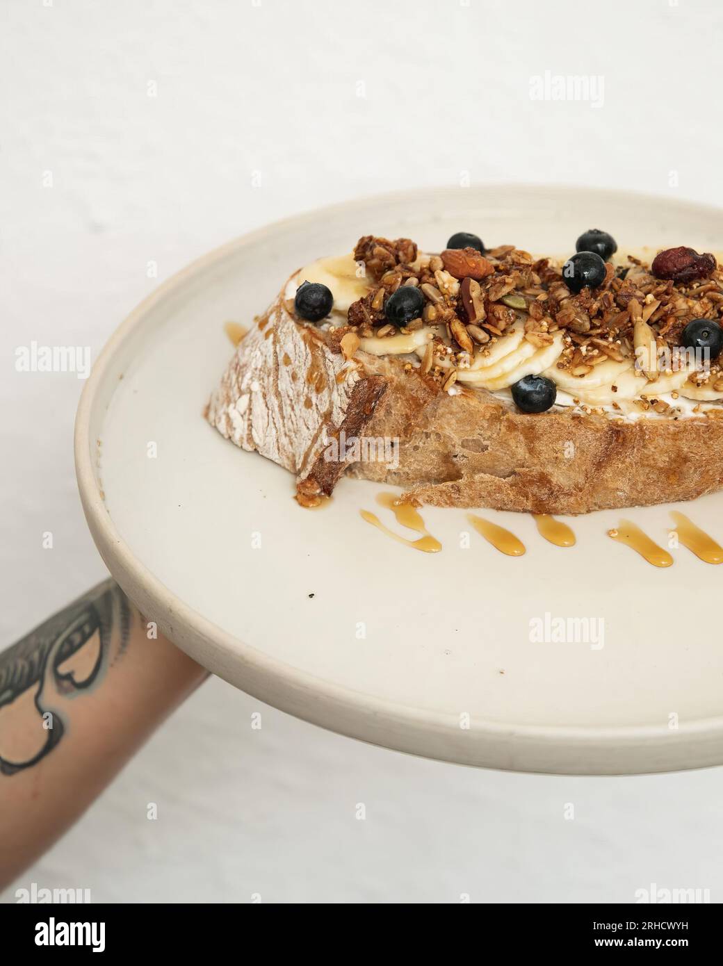 dulce in padella con banana, noce di mora e mandorla, immersa nel miele, su un piatto di ceramica bianca con una piastra di supporto per il braccio Foto Stock