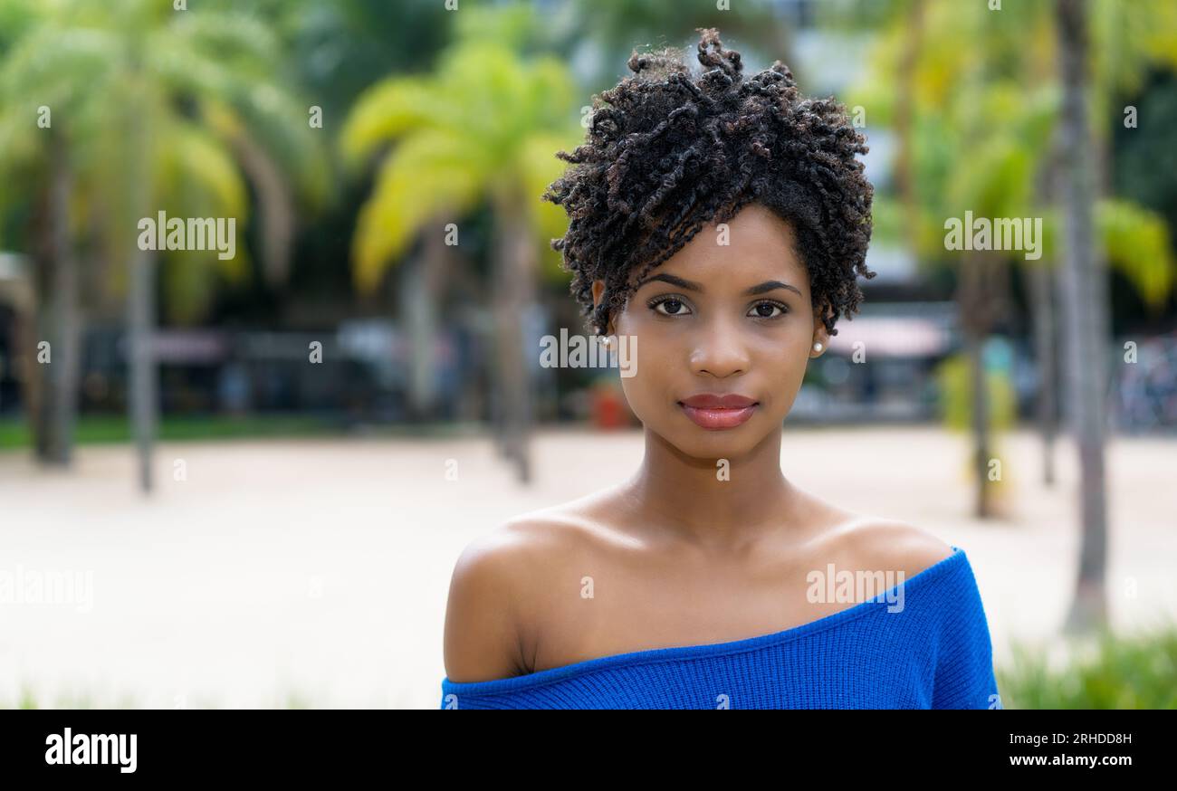 Bella donna afroamericana giovane adulta con capelli ricci all'aperto con palme Foto Stock