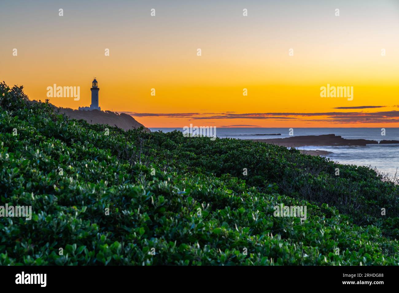 Alba con la riva bassa delle nuvole e il faro di Norah Head da Soldiers Beach sulla costa centrale, New South Wales, Australia. Foto Stock