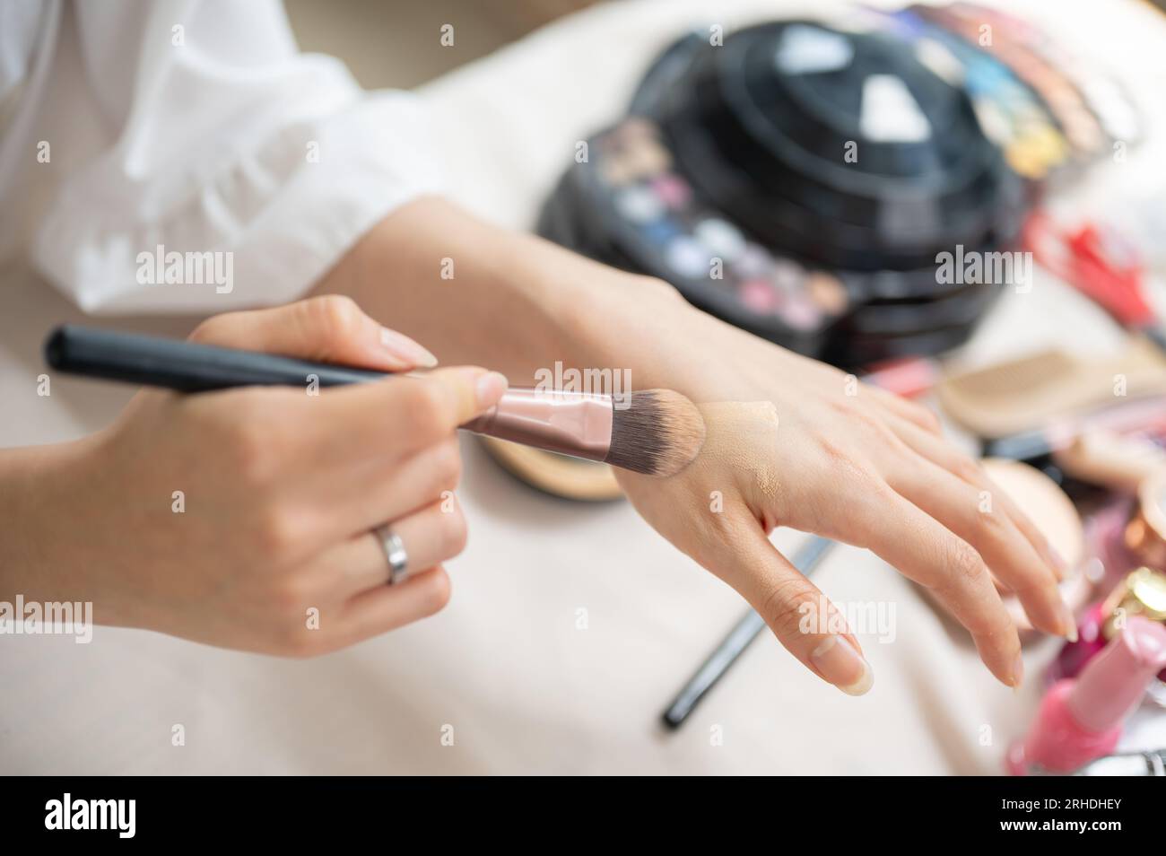Immagine ravvicinata con vista dall'alto di una makeup artist o beauty influencer che applica fondamenti alla sua mano con un pennello per il trucco. cosmetici, cura della pelle, bellezza Foto Stock
