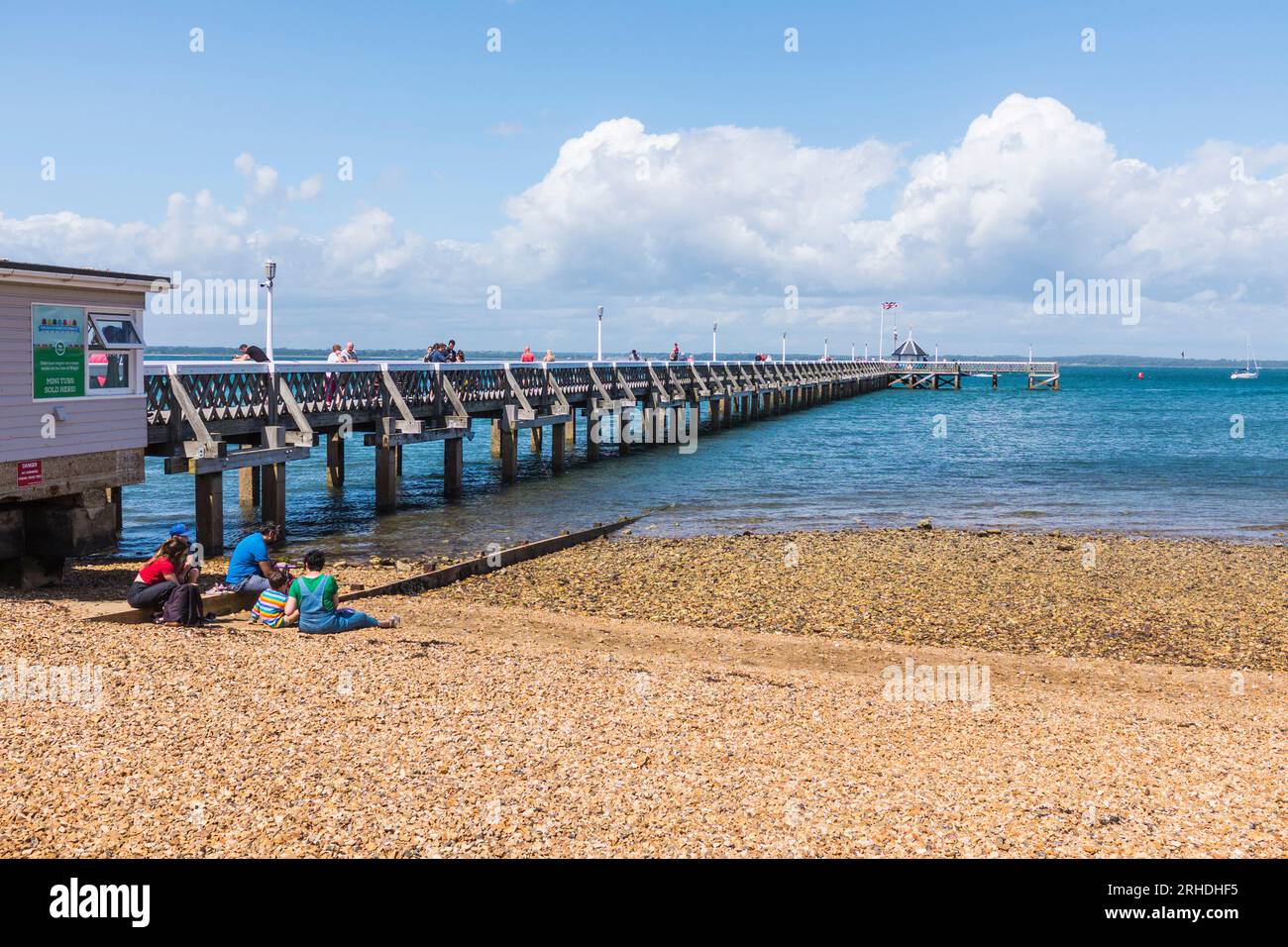 La gente si sedeva sulla spiaggia godendosi il sole vicino al molo di Yarmouth, Isola di Wight, Inghilterra, Regno Unito Foto Stock