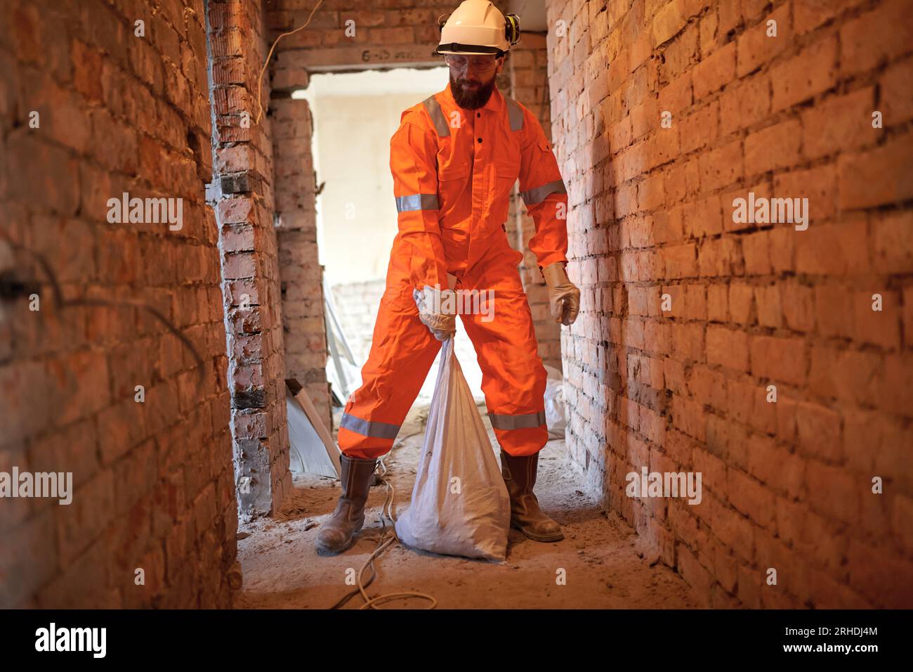 Operaio edile che trasferisce manualmente i rifiuti in sacchetti di zucchero in loco. Foto Stock