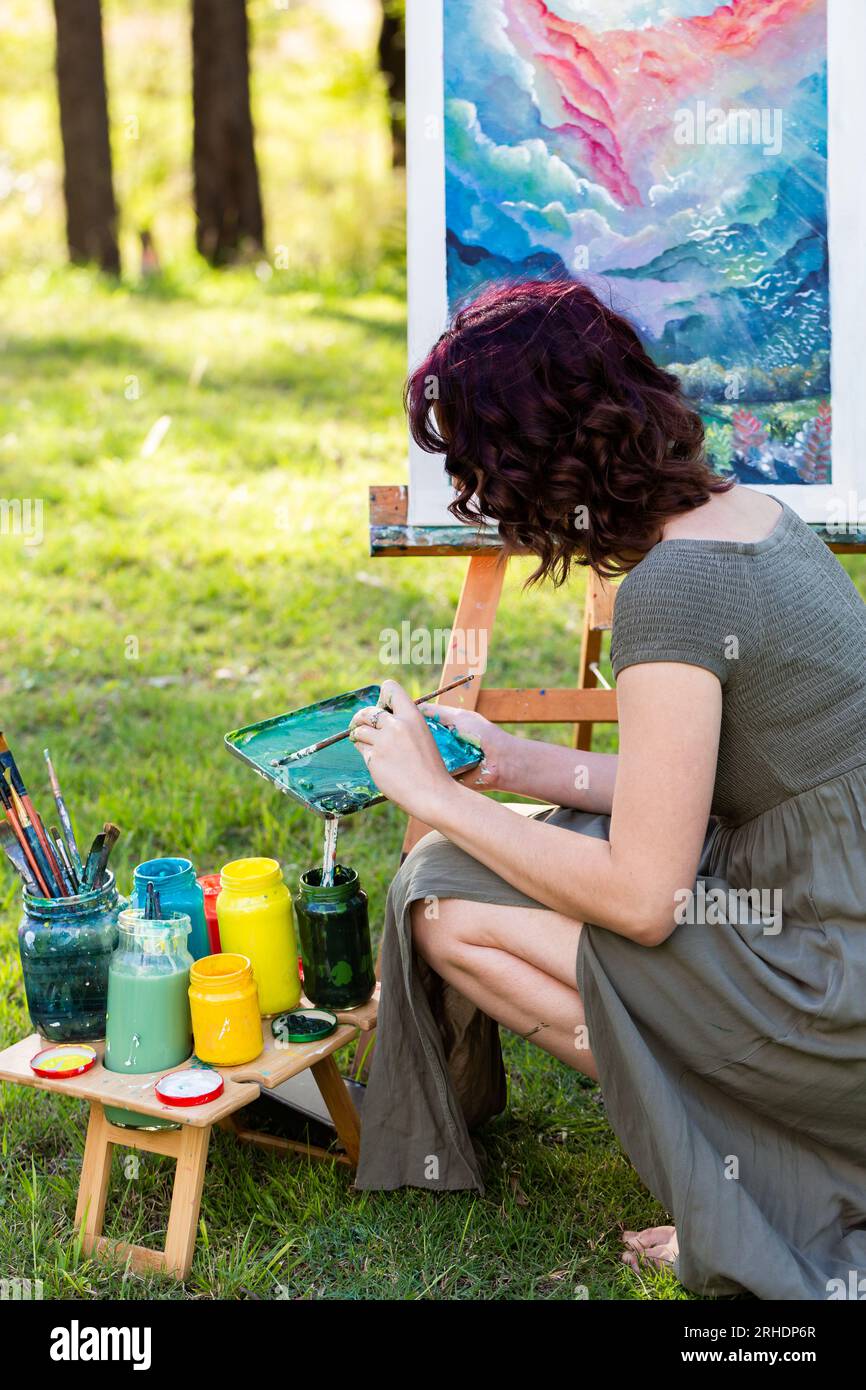 Giovane artista australiano che mescola colori per opere d'arte acriliche mentre dipinge all'aperto Foto Stock
