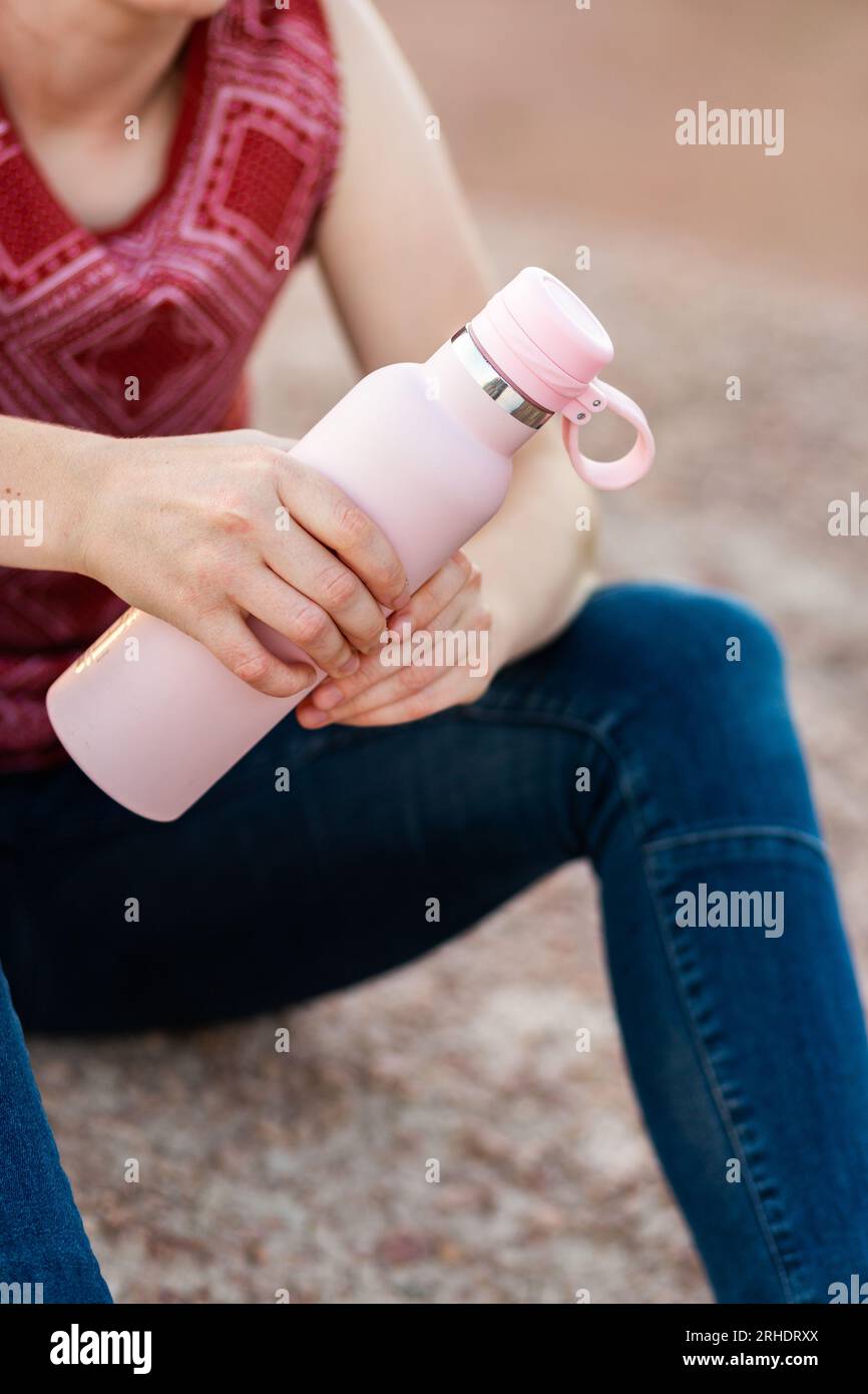 Bottiglia da bibita riutilizzabile in mani di donna seduta a terra dopo una passeggiata, piena di acqua rinfrescante Foto Stock