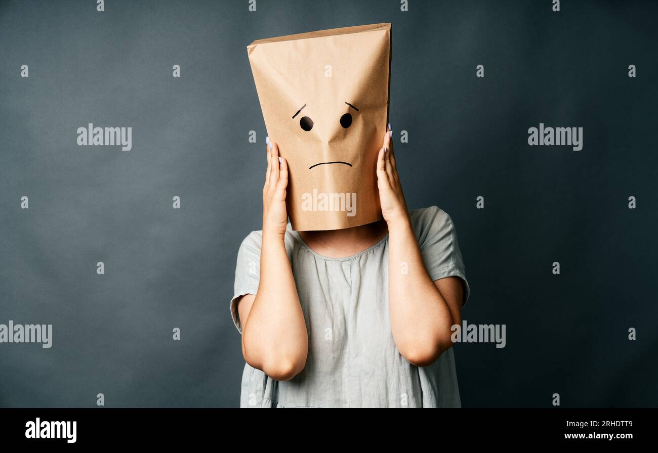 Una donna sconvolta con un sacchetto di carta sulla testa che tocca le tempie, soffre di forte cefalea tesa su sfondo grigio. Concetto di emozione Foto Stock