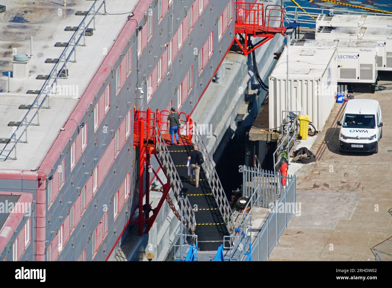 Persone che salgono sulla chiatta dell'alloggio Bibby Stockholm al porto di Portland nel Dorset dopo che è stata dichiarata sicura. I richiedenti asilo sono stati messi a bordo della chiatta lunedì scorsa settimana, ma sono stati rimossi venerdì dopo i test hanno rivelato la Legionella - i batteri che possono causare la malattia dei Legionari potenzialmente fatale. Data foto: Mercoledì 16 agosto 2023. Foto Stock