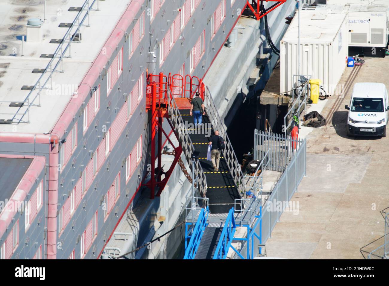 Persone che salgono sulla chiatta dell'alloggio Bibby Stockholm al porto di Portland nel Dorset dopo che è stata dichiarata sicura. I richiedenti asilo sono stati messi a bordo della chiatta lunedì scorsa settimana, ma sono stati rimossi venerdì dopo i test hanno rivelato la Legionella - i batteri che possono causare la malattia dei Legionari potenzialmente fatale. Data foto: Mercoledì 16 agosto 2023. Foto Stock