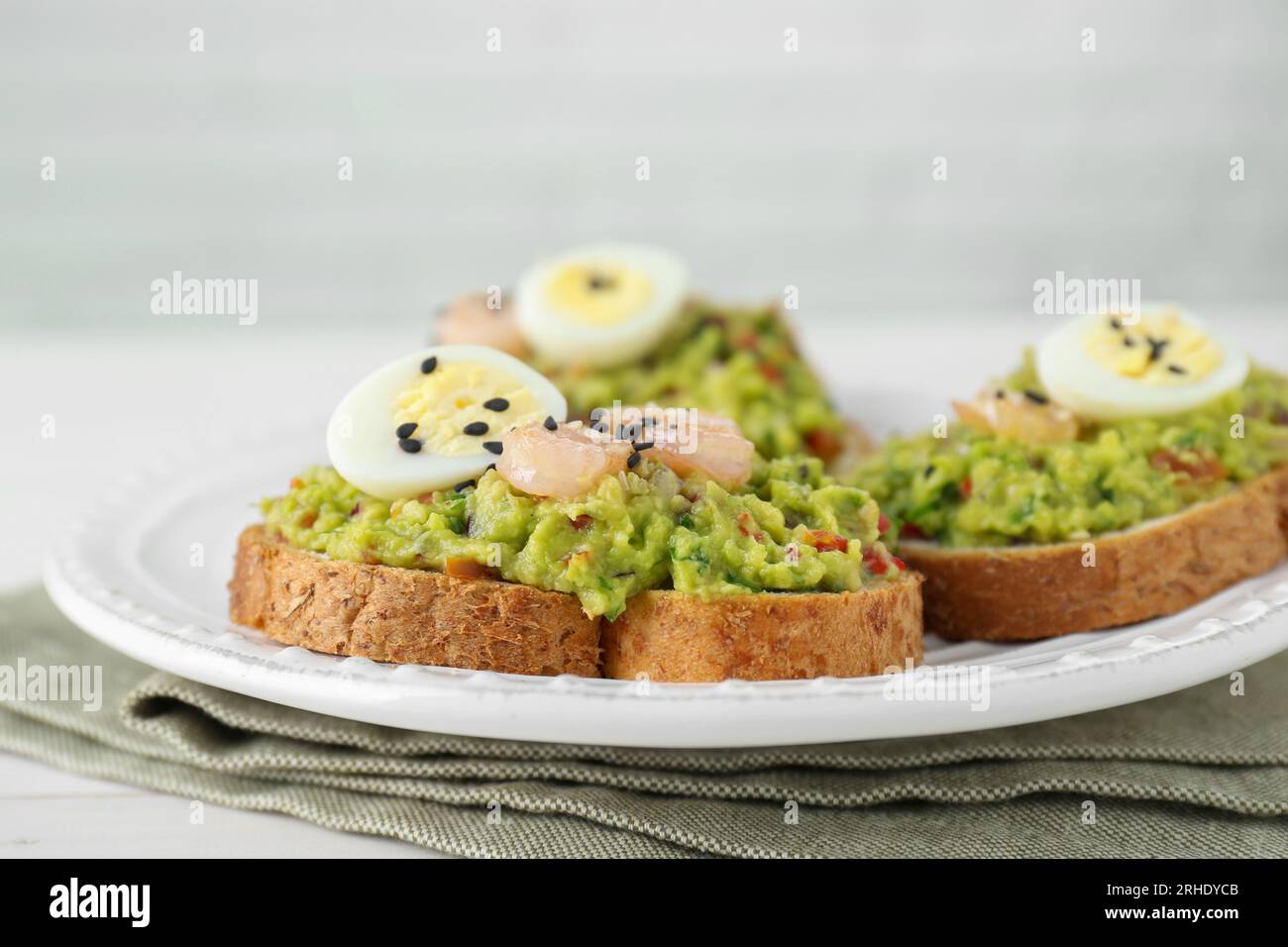 Fette di pane con guacamole saporito, uova e gamberi sul tavolo, primo piano Foto Stock