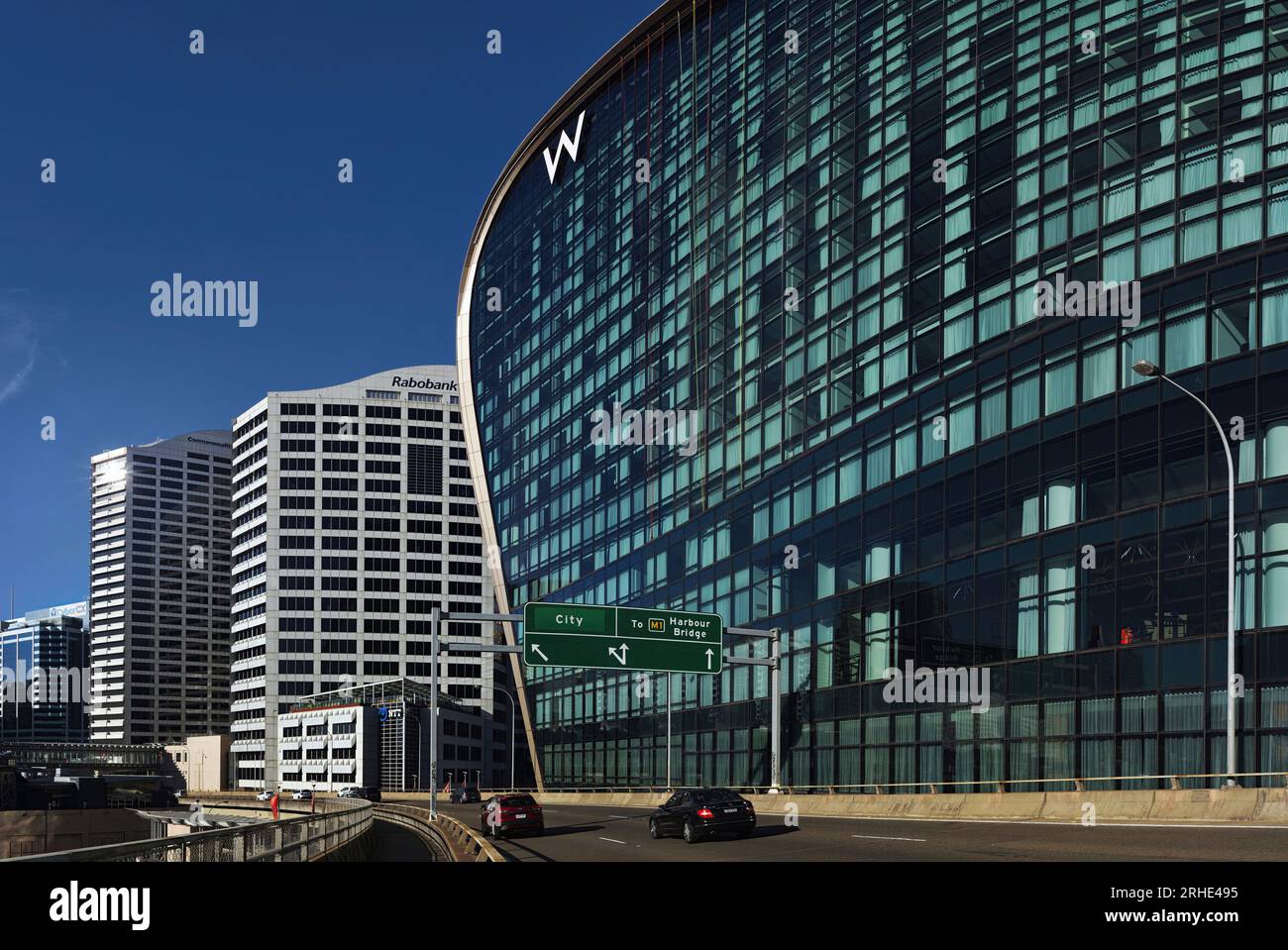 La massiccia distesa della parete di vetro curva del W Sydney Hotel, Darling Harbour. Fotografia architettonica ad alta risoluzione, logo W e cielo azzurro Foto Stock