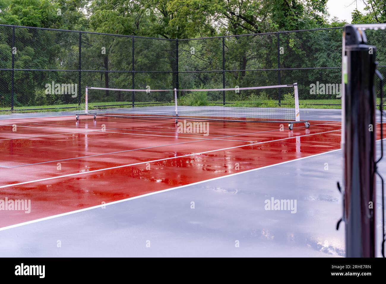 Nuove reti portatili per picchieri su un campo da tennis bagnato rosso con linee bianche combinate con linee grigie per picchieri Foto Stock