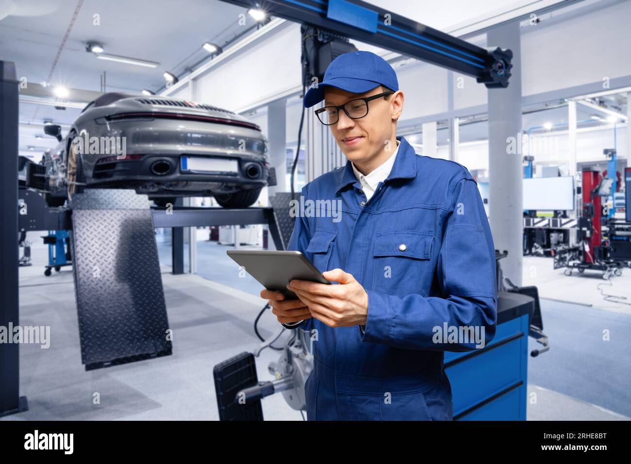 Addetto alla manutenzione con tablet digitale sullo sfondo dell'auto nel servizio auto. Foto Stock