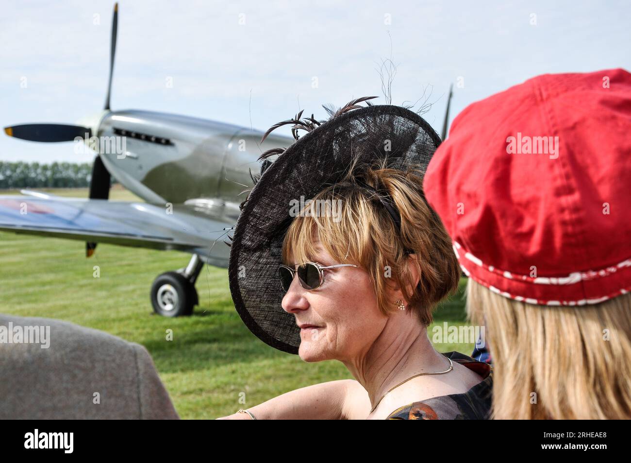 Donna in abbigliamento d'epoca che guarda l'esibizione aerea all'evento vintage Goodwood Revival, West Sussex, Regno Unito. Aereo Spitfire. Bel cappello nero, fascinatore Foto Stock
