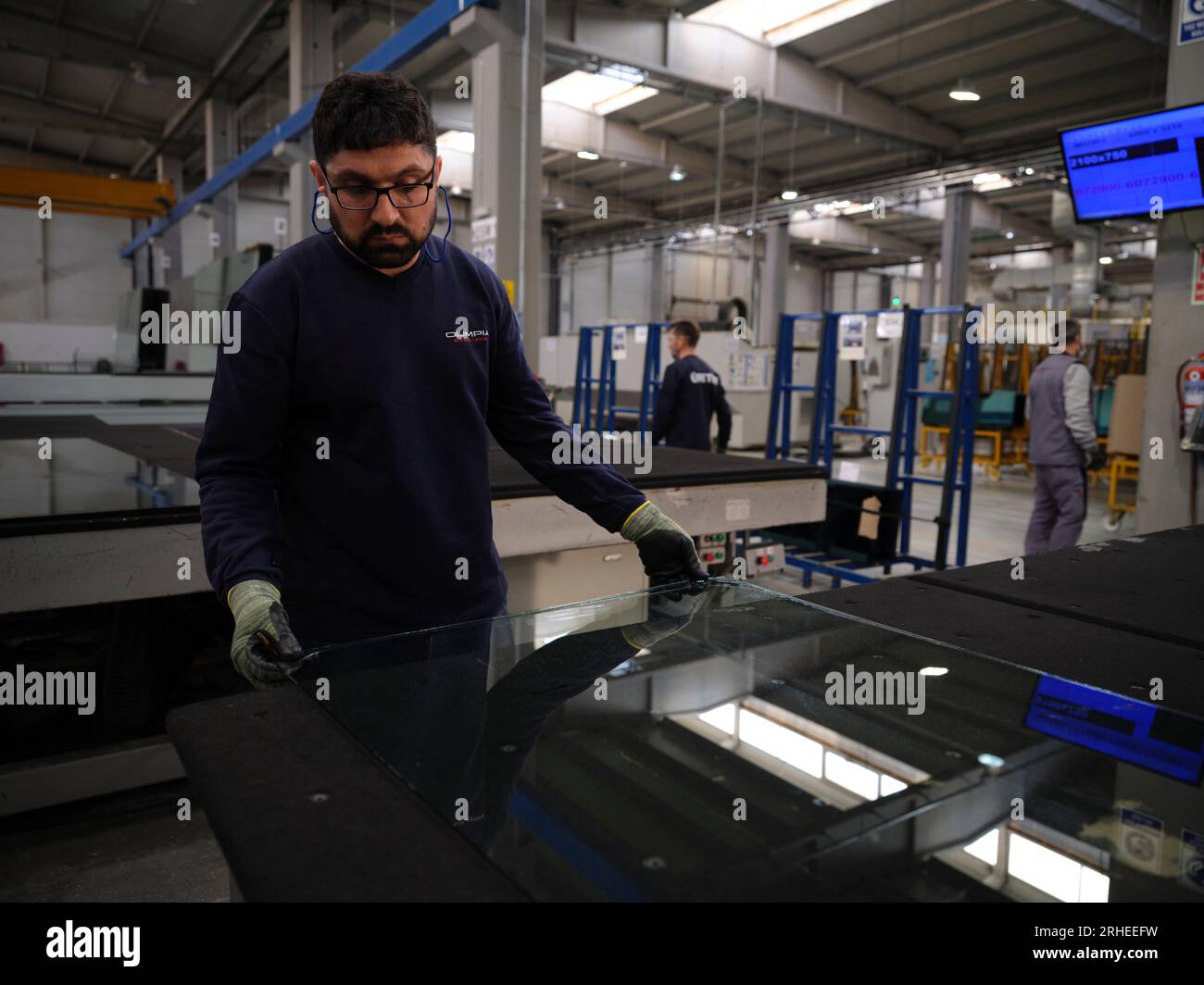 Fabbrica per la produzione di finestrini e parabrezza per auto. Lavoratore manuale che assembla finestre in PVC e finestrini per auto. Lavoratori che confezionano fogli di vetro in magazzino Foto Stock