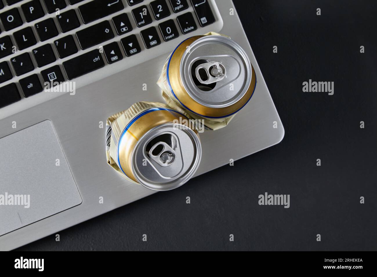 Due lattine vuote di birra in alluminio schiacciate su un computer portatile su un tavolo nero. Combattimenti ubriachi sui social media Foto Stock