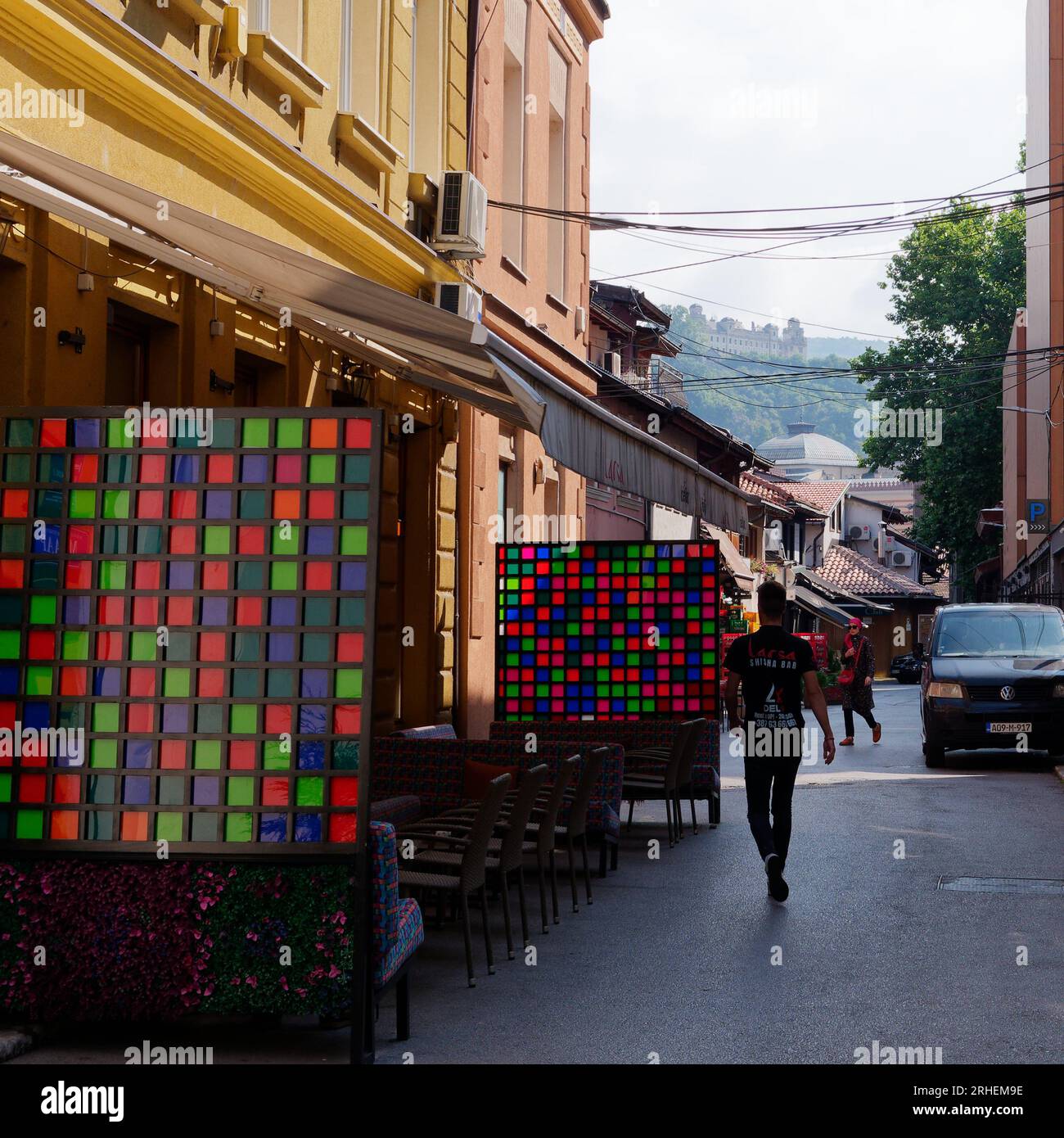 Caffè con tavole divisorie multicolore mentre il personale passeggia, fortezza sullo sfondo nella città di Sarajevo, Bosnia ed Erzegovina, 16 agosto 2023. Foto Stock