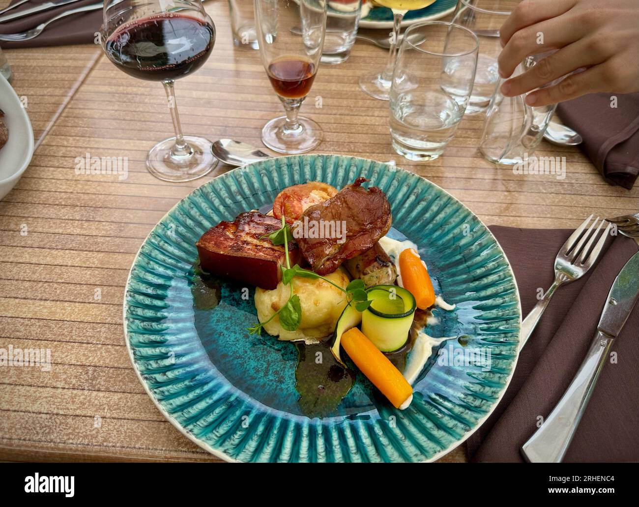 Delizie gastronomiche: Colorato pasto di maiale presso un ristorante, servito su un piatto blu con vino Foto Stock