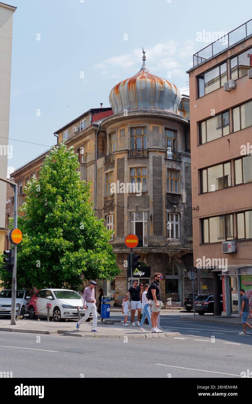 La gente cammina lungo una strada nella nuova parte di Sarajevo in un giorno estivo con un caratteristico edificio ad angolo con cupola , Bosnia ed Erzegovina, 16 agosto 2023. Foto Stock