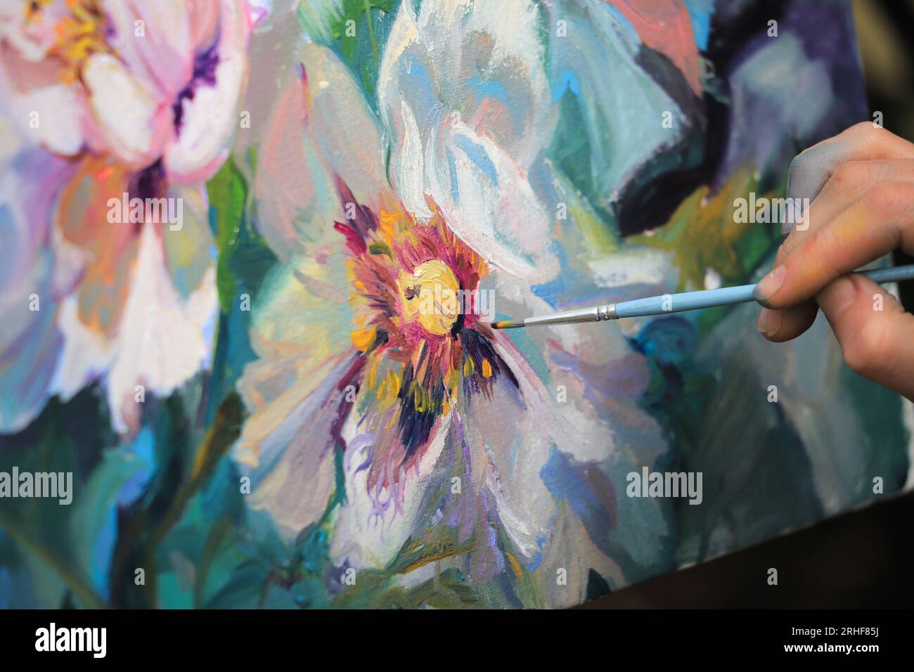 L'artista dipinge un quadro con i fiori in primo piano con un pennello Foto Stock