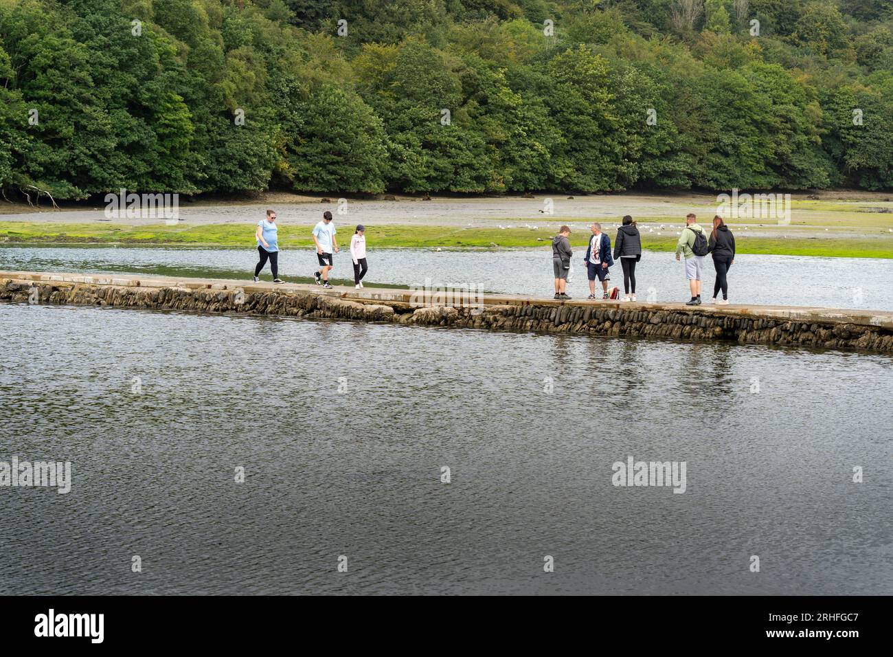 Looe, Regno Unito - agosto 2023: Turisti che camminano lungo la piscina di Mill, vicino a Looe in Cornovaglia con l'estuario del fiume Looe sullo sfondo Foto Stock