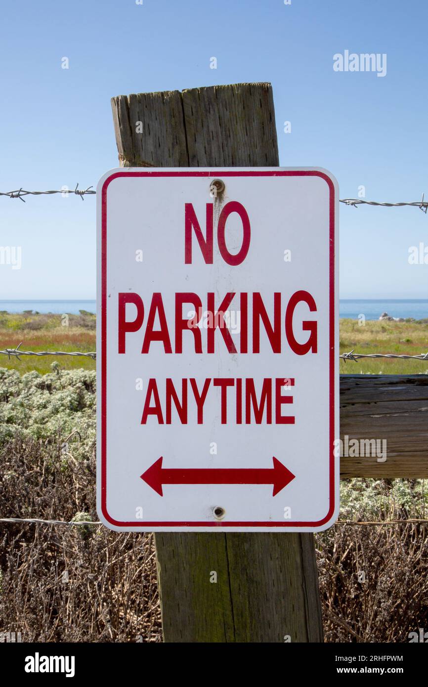 Non è consentito parcheggiare in qualsiasi momento sulla recinzione con filo spinato. Nessun cartello per parcheggiare con la costa oceanica sullo sfondo. Non è consentito parcheggiare all'aperto in qualsiasi momento. Disposizione verticale Foto Stock