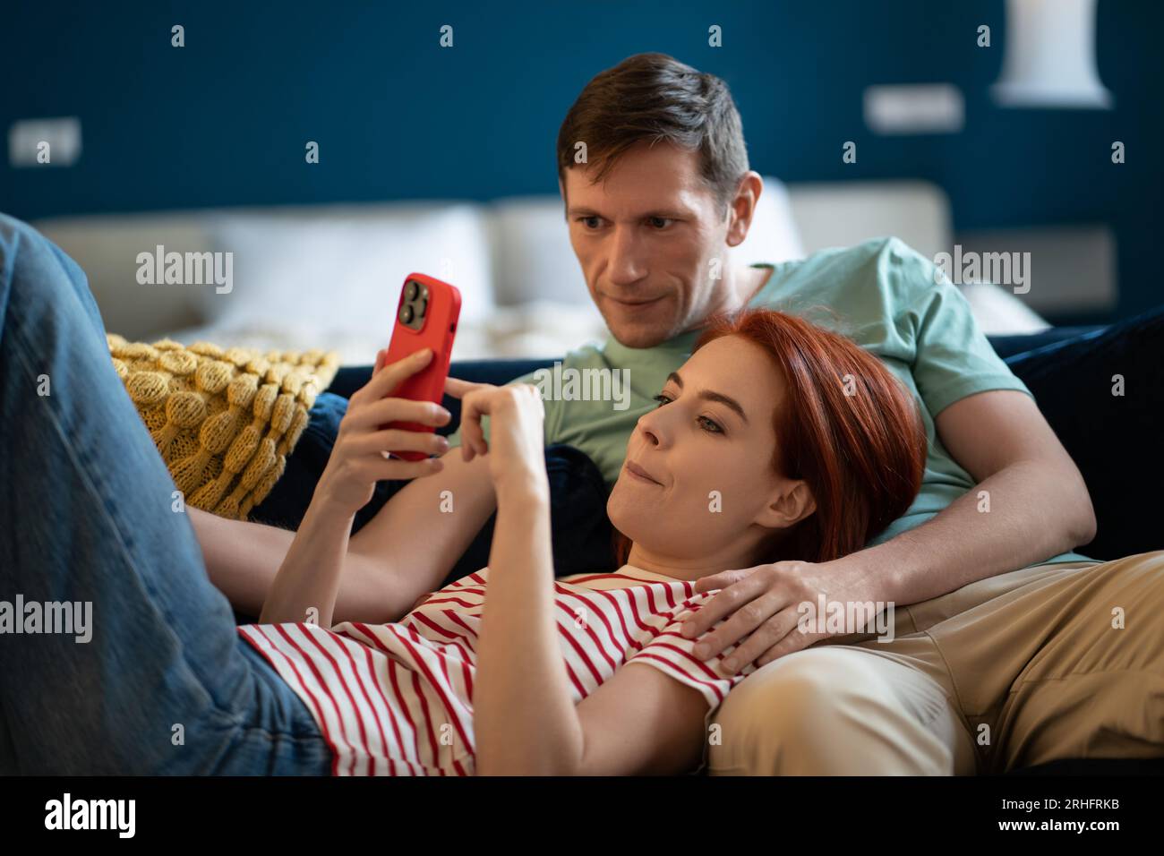 Coppia di mezza età soddisfatta e ben riposata che si rilassa sul divano a casa riposando con lo smartphone. Foto Stock