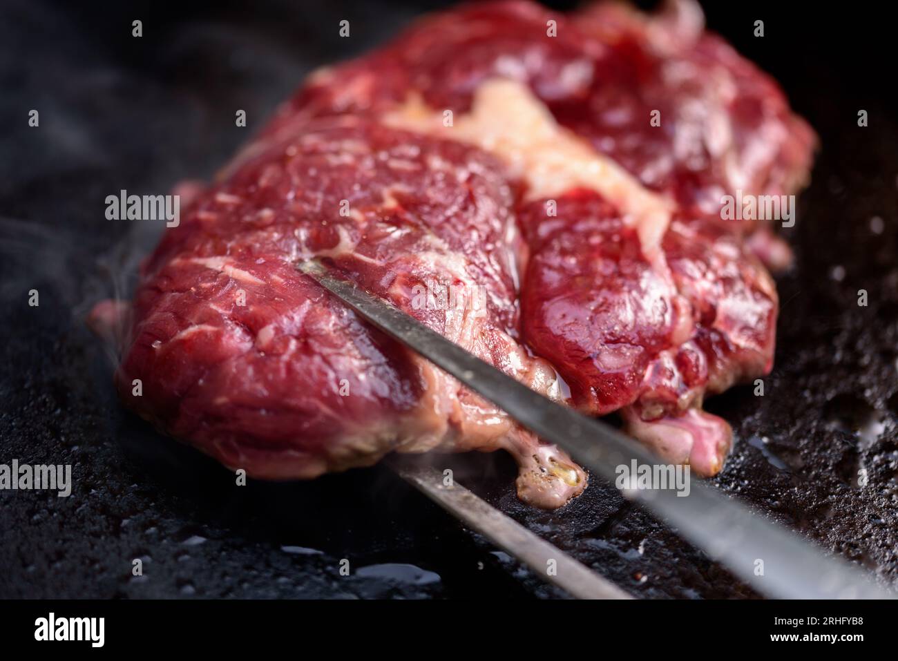 Chef che cucina bistecche su un grill con affumicato che sfrigolava il grill. Foto Stock
