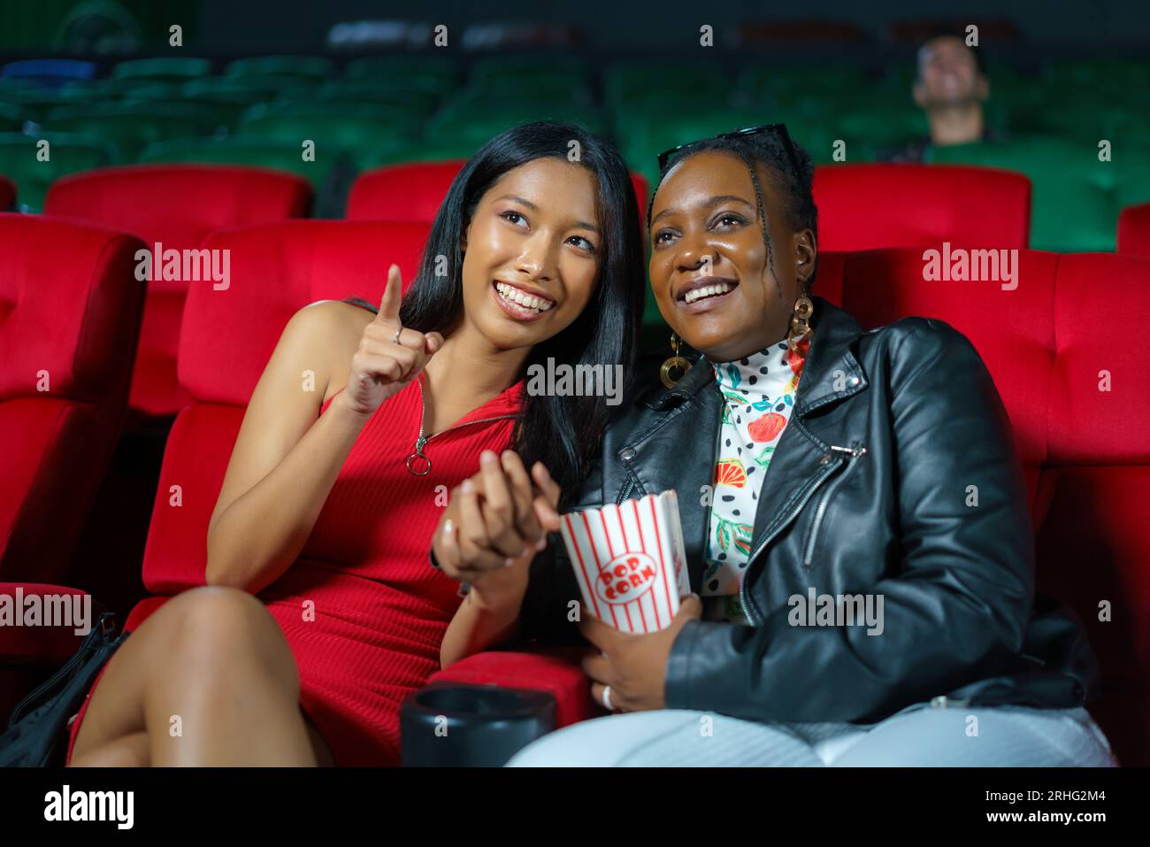 Le lesbiche gioiose condividono un sorriso mentre guardano un film al cinema, godendosi un'esperienza cinematografica coinvolgente e inclusiva insieme. Foto Stock