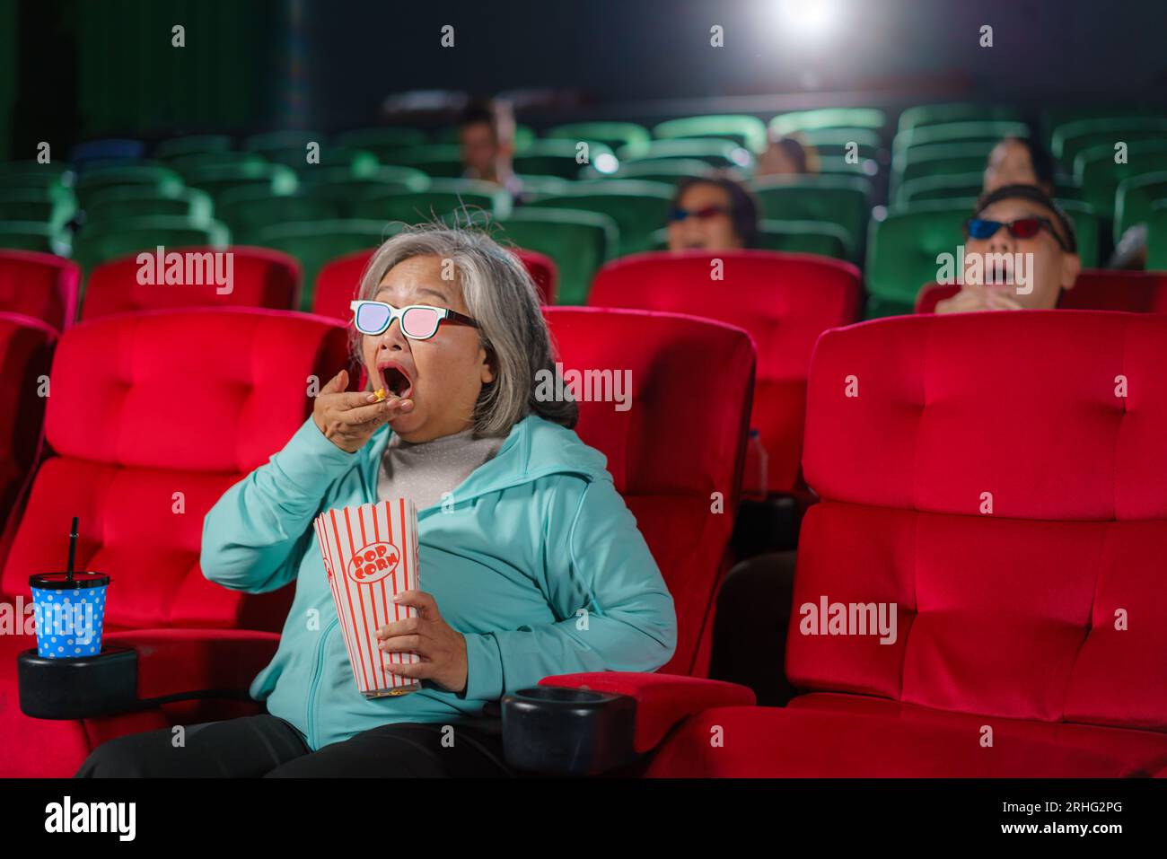 Le donne anziane asiatiche con gli occhiali guardano con entusiasmo film 3D, popcorn in mano, per vivere un'esperienza coinvolgente. Foto Stock