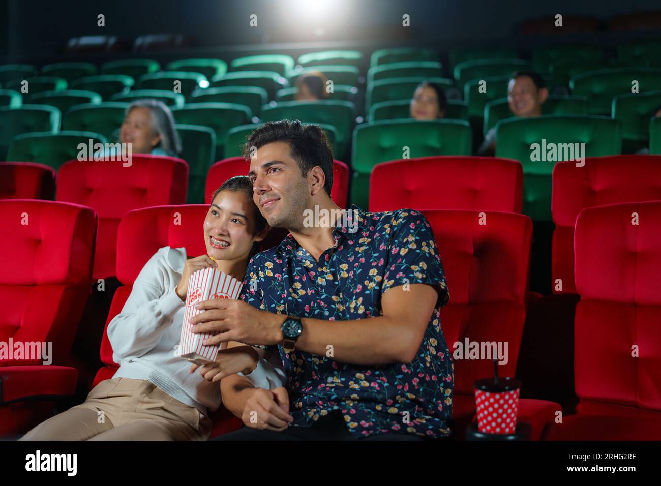 Le coppie si divertono guardando i film mentre tengono popcorn, creando un'esperienza serale al cinema accogliente e divertente. Foto Stock