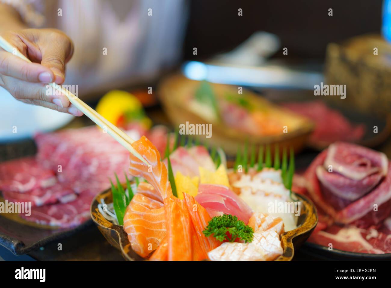 Una donna indossa le bacchette per mettere delicatamente il sashimi di salmone fresco su un piatto in un ristorante giapponese, catturando l'arte culinaria. Foto Stock