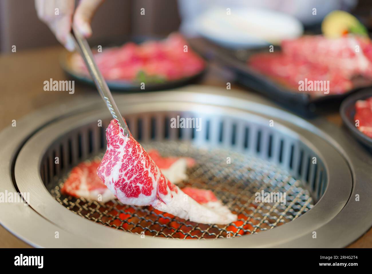 Woman's Hand utilizza pinze per posizionare il wagyu beef su un piatto, pronto per grigliare su carbone, migliorando l'esperienza culinaria in un ristorante giapponese Foto Stock