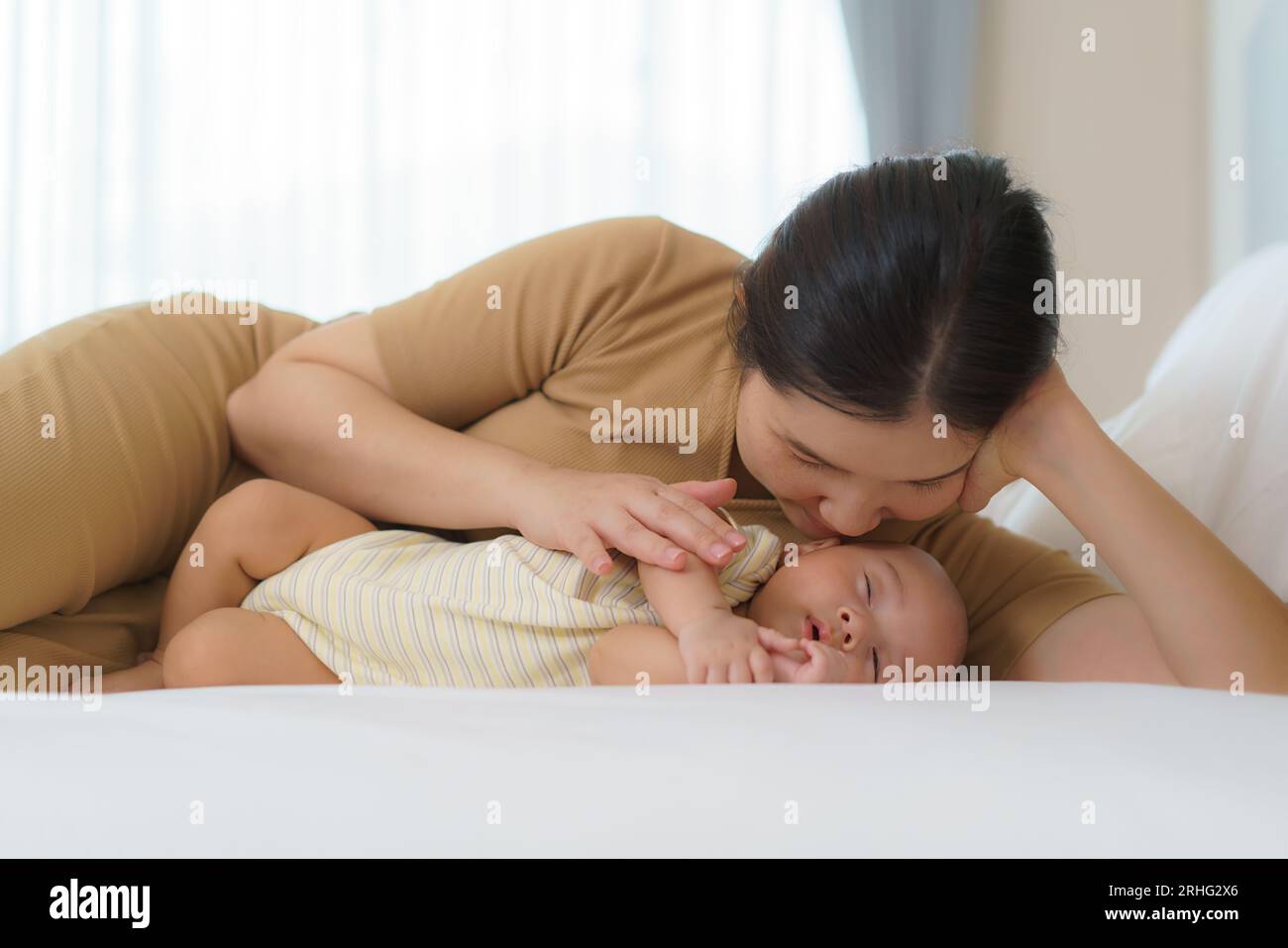 La madre asiatica abbracciò il suo giovane figlio in modo che potesse dormire bene in camera da letto a casa, rappresenta l'amore e la famiglia Foto Stock