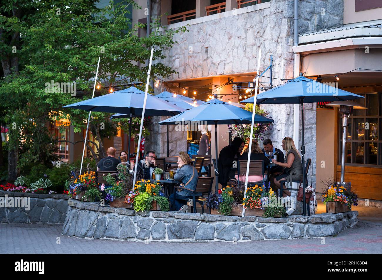 I turisti cenano all'aperto la sera d'estate nei patio del ristorante nel villaggio di Whistler. Whistler BC, Canada. Foto Stock