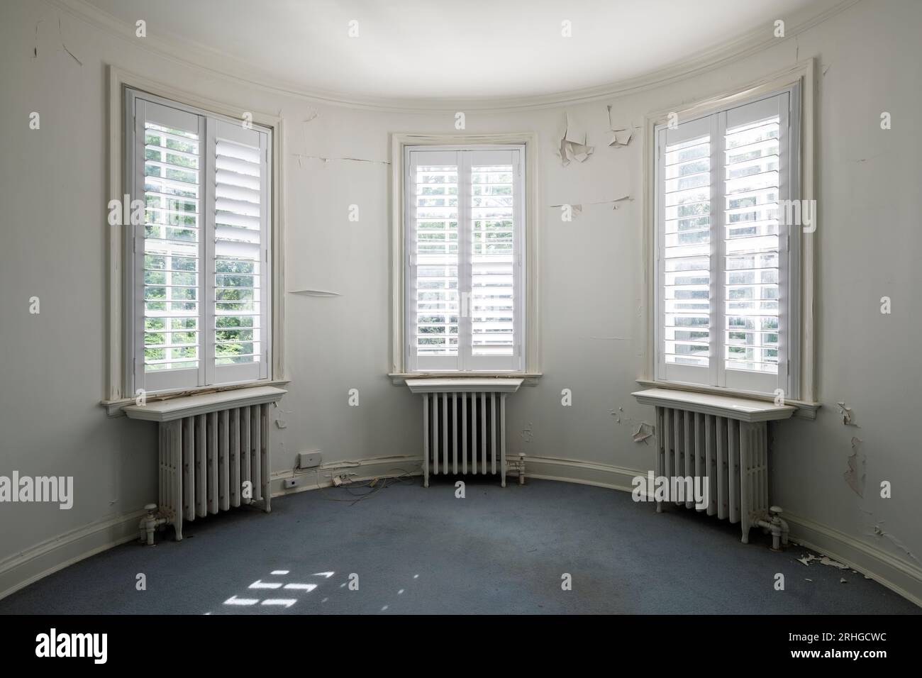 Un trio di finestre all'interno di una stanza che ha una parete curva all'interno di una casa abbandonata. Foto Stock