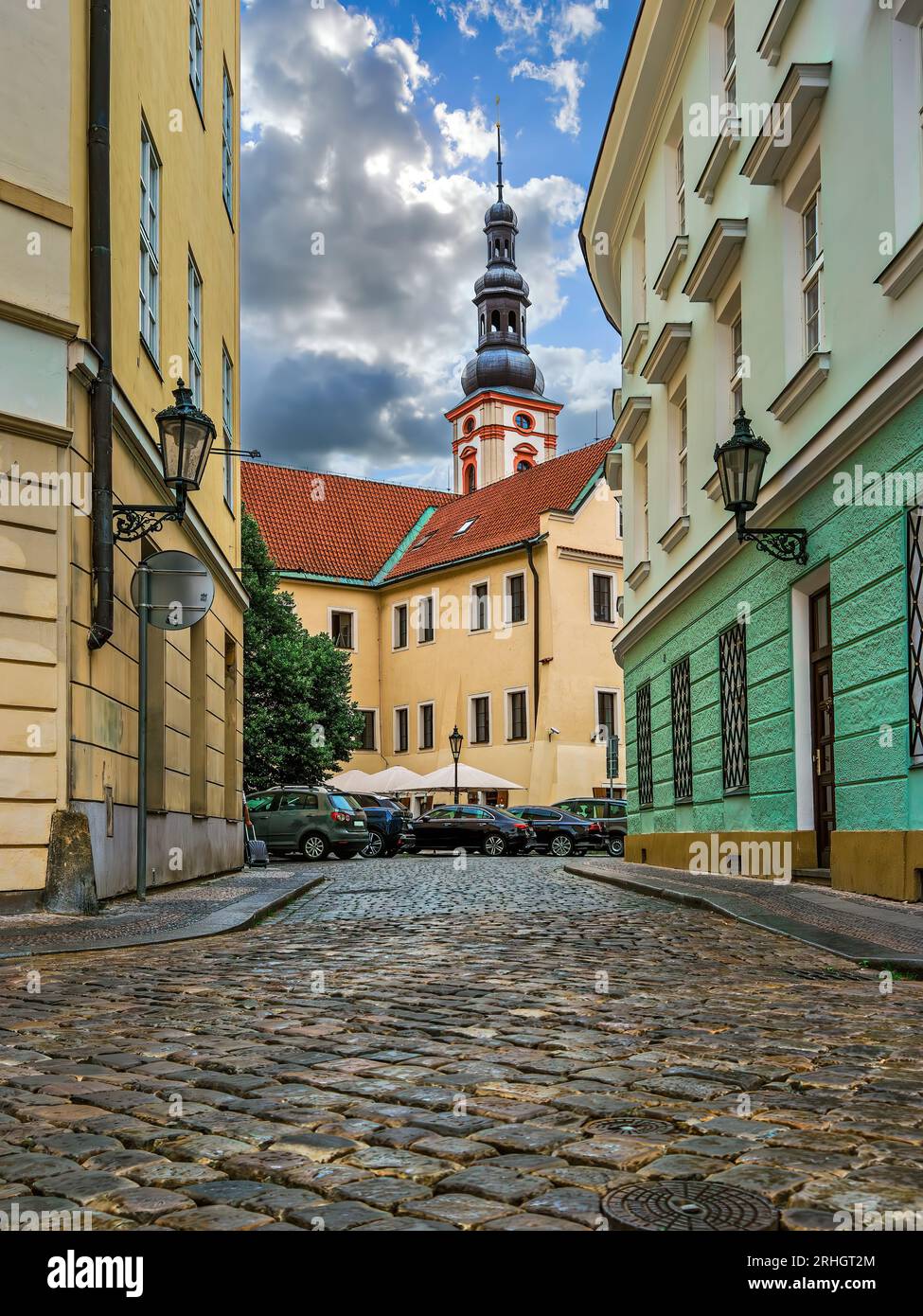 Stretta strada acciottolata tra edifici colorati come una chiesa cattolica sullo sfondo nella città vecchia di Praga, Repubblica Ceca. Foto Stock