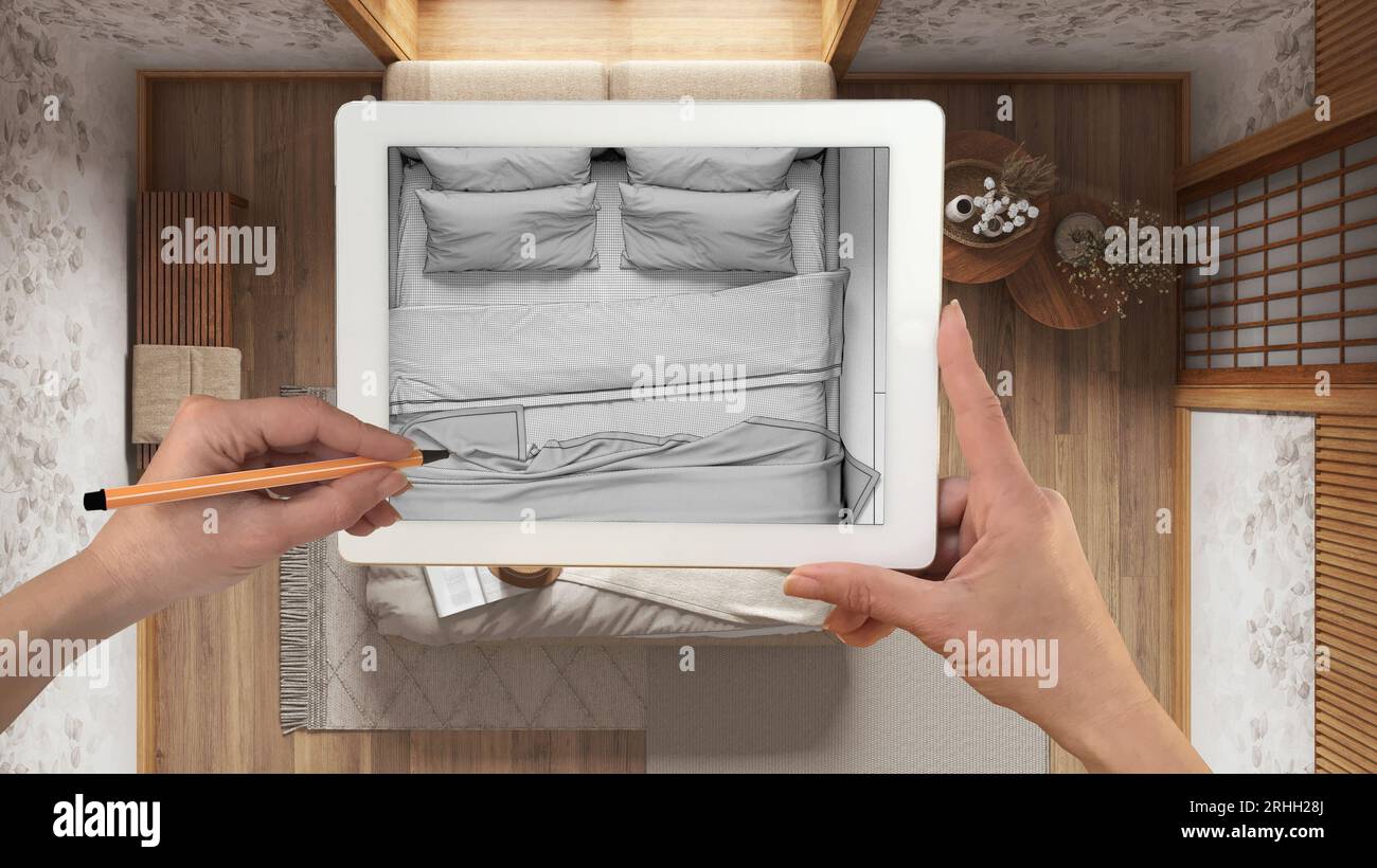 Mani che reggono e disegnano su un tablet che mostra il moderno disegno CAD della camera da letto dei japandi in legno. Interni rifiniti sullo sfondo, design architettonico pr Foto Stock