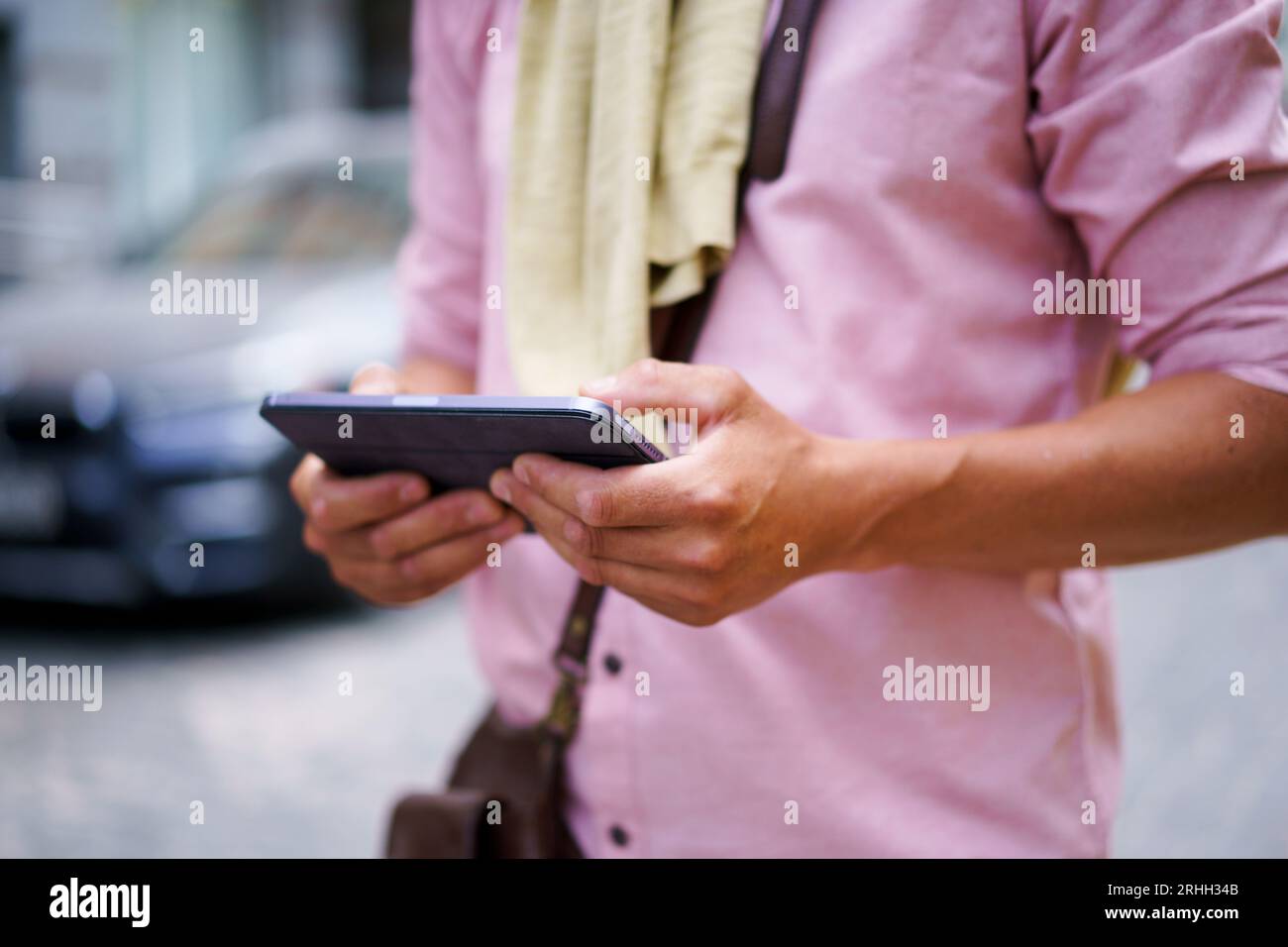 Immagine ravvicinata, il concetto di comunicazione digitale prende vita mentre le mani dell'uomo tengono sapientemente il tablet PC sulla trafficata strada della città. La prospettiva ravvicinata evidenzia i dettagli del dispositivo touchscreen, sottolineandone il ruolo nel facilitare la comunicazione moderna e l'accesso alle informazioni. Foto di alta qualità Foto Stock