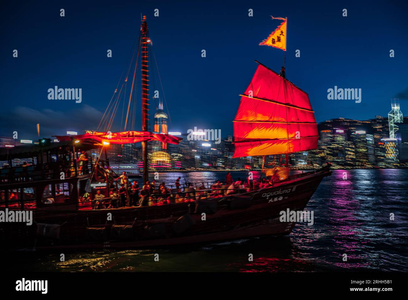 Splendida vista notturna di una junk boat luminosa nel Victoria Harbour di fronte al fantastico skyline di Hong Kong con i suoi impressionanti grattacieli Foto Stock