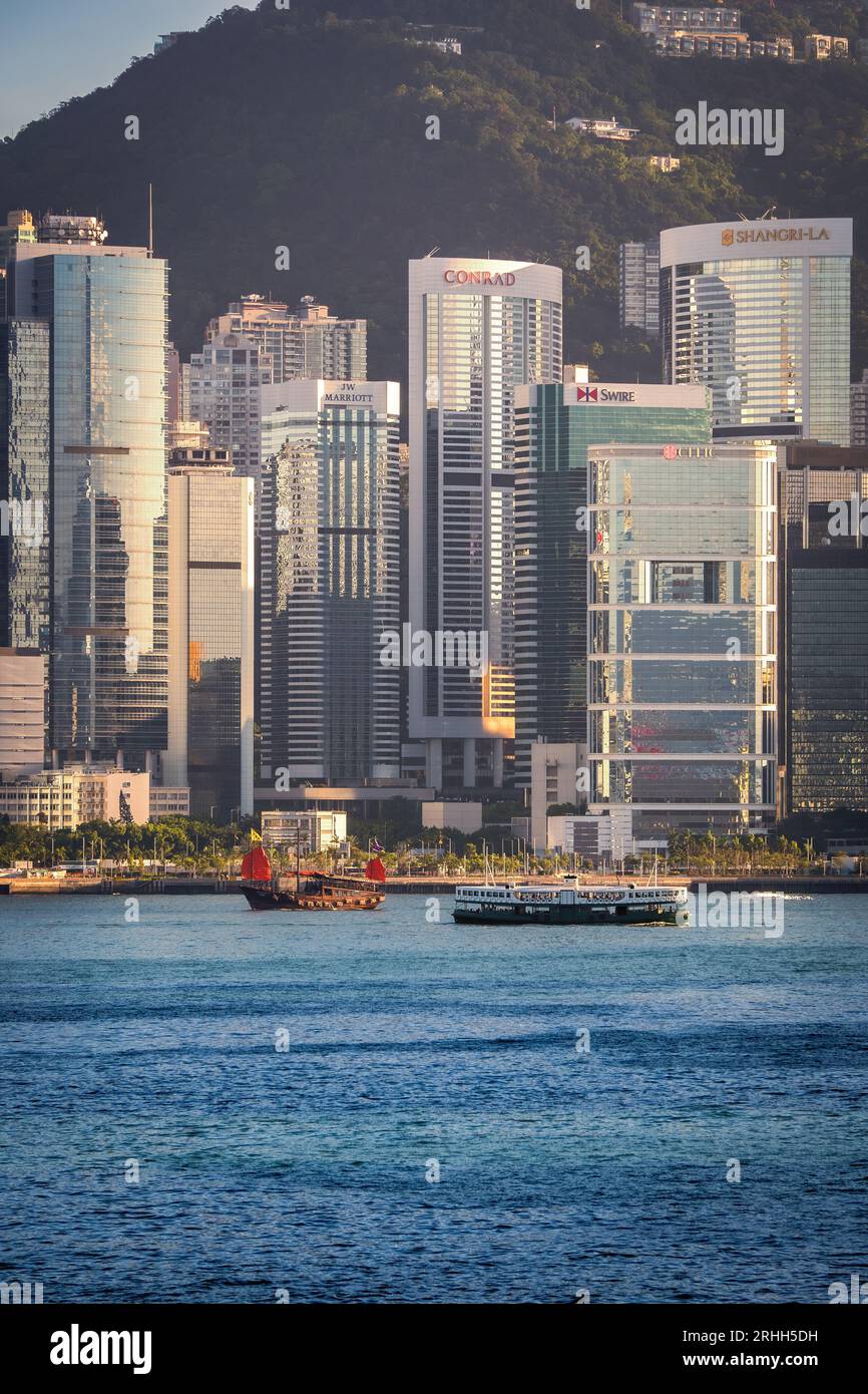 Splendida vista diurna di una vecchia barca spazzatura e di un traghetto, navigando attraverso Victoria Harbour di fronte agli alti grattacieli di Hong Kong, sar, Cina Foto Stock
