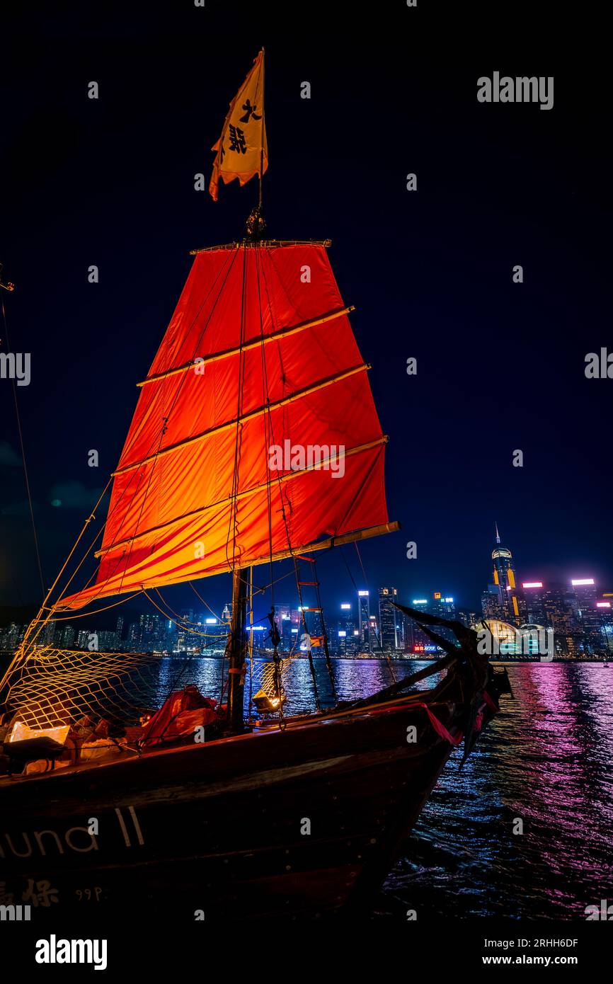 Fantastica vista notturna di una giunca luminosa nel Victoria Harbour di fronte al fantastico skyline di Hong Kong con i suoi impressionanti grattacieli Foto Stock