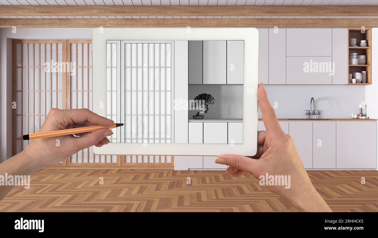 Mani che tengono e disegnano su un tablet che mostra una cucina bianca minimale, disegno CAD dettagliato. Interni con finiture reali sullo sfondo, design architettonico p Foto Stock