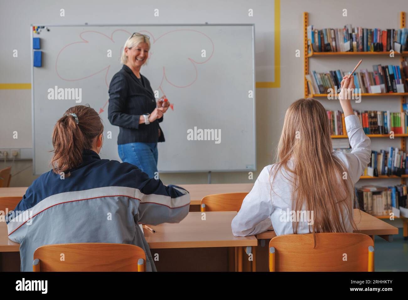 Due studentesse delle scuole superiori partecipano attivamente alla classe, volendo rispondere alle domande e alzare la mano Foto Stock