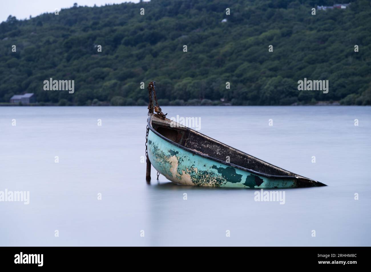 Piccola imbarcazione parzialmente sommersa legata a un palo in un lago. L'esposizione prolungata conferisce un effetto uniforme alla superficie dell'acqua. Foto Stock