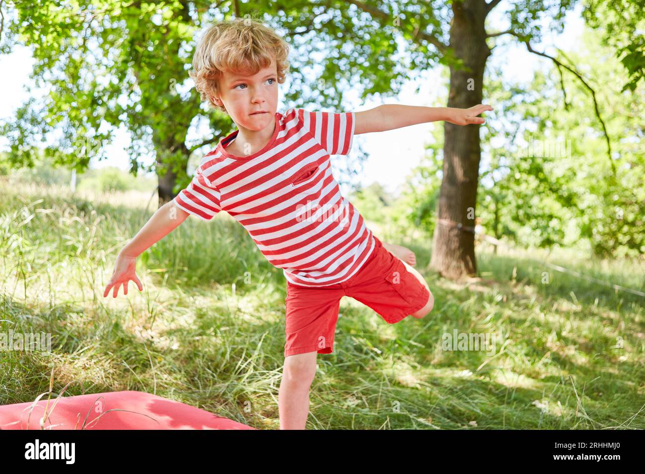 Ragazzo biondo che guarda lontano mentre si trova in equilibrio in giardino Foto Stock
