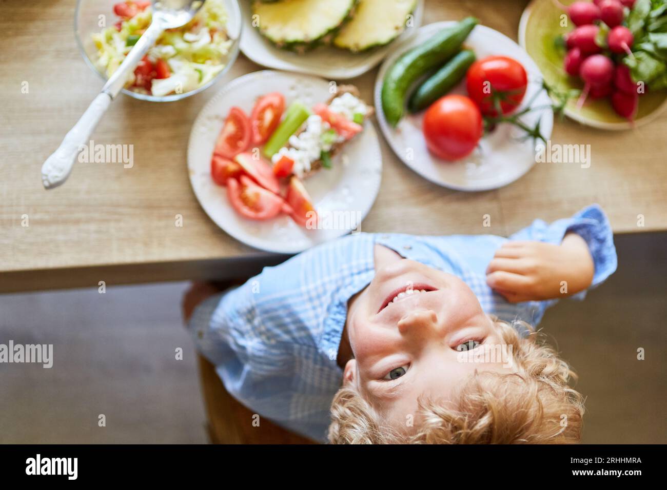 Ritratto di un ragazzo sorridente che guarda in alto con frutta e verdura sul tavolo a casa Foto Stock