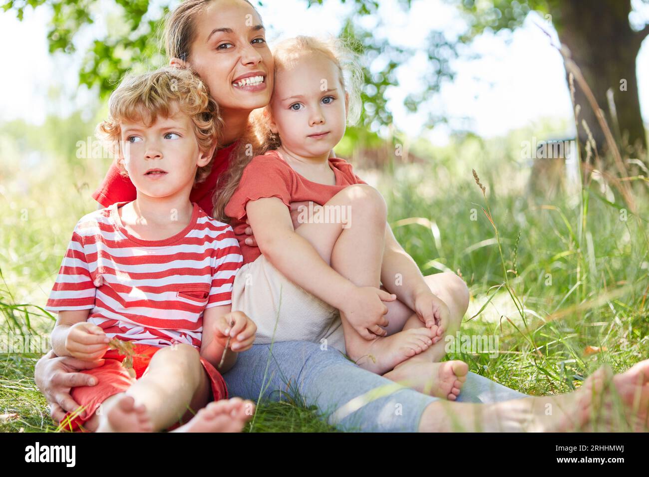 Ritratto di madre felice seduta con figlio e figlia sull'erba in giardino Foto Stock