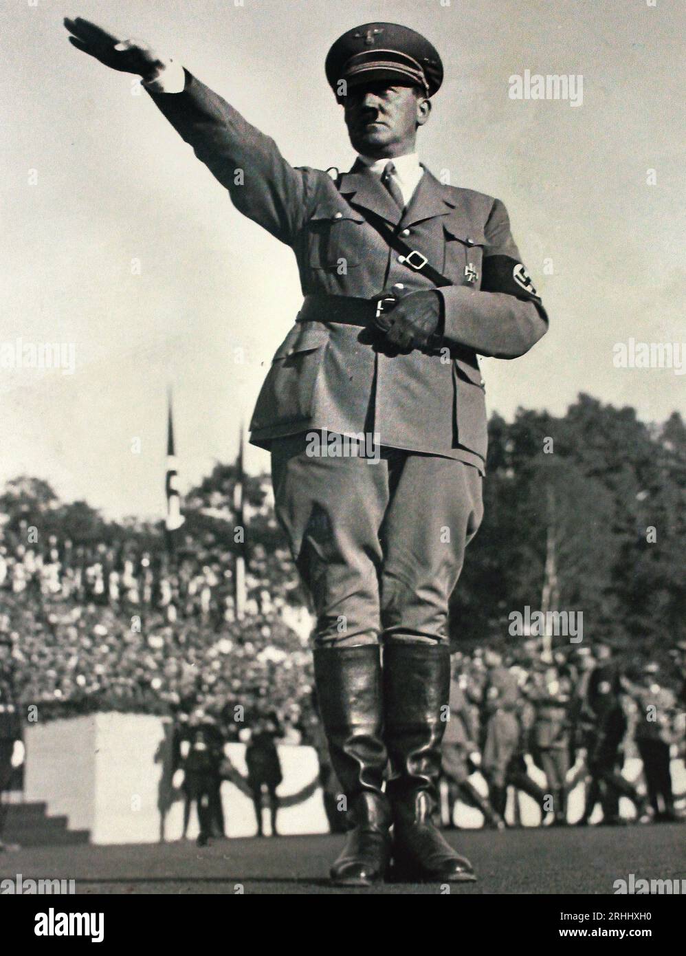 Foto storica degli anni '30 che mostra Adolf Hitler in uniforme che fa il saluto nazista durante un'enorme manifestazione politica, Germania nazista. Adolf Hitler che fa il saluto nazista mentre è in uniforme a un'enorme manifestazione politica all'aperto, tipica delle Adunate di Norimberga (Reichsparteitag) tenute negli anni '30. Indossa un berretto militare con visiera, un bracciale NSDAP con una svastica, una cintura a croce e stivali alti in pelle nera, in piedi davanti a una grande folla di spettatori e membri del partito in uniforme. Foto Stock