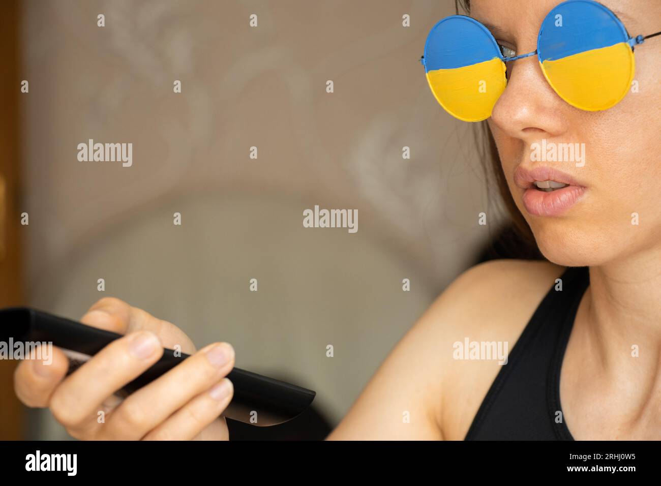 La bandiera dell'Ucraina sugli occhiali di una ragazza che guarda la TV a casa con un telecomando nelle sue mani, un patriota Foto Stock