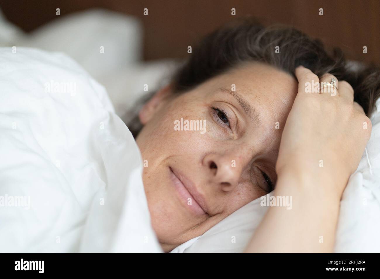 Donna stanca di 52 anni in un letto in un hotel Foto Stock