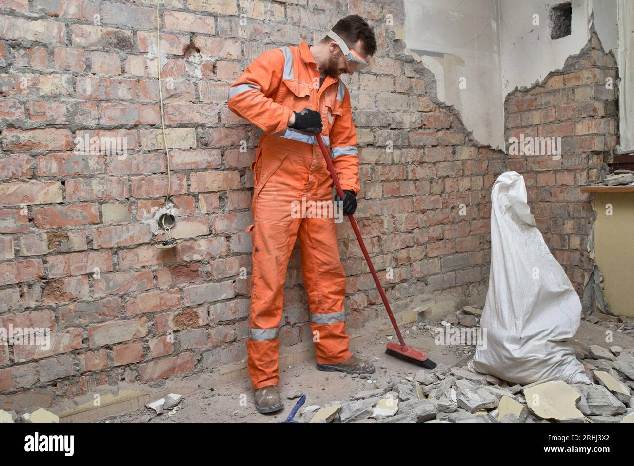Camera per la pulizia di edifici in cemento vecchio e mattoni dopo lavori di demolizione, indossando guanti, maschere, stivali e tute arancioni. Foto Stock
